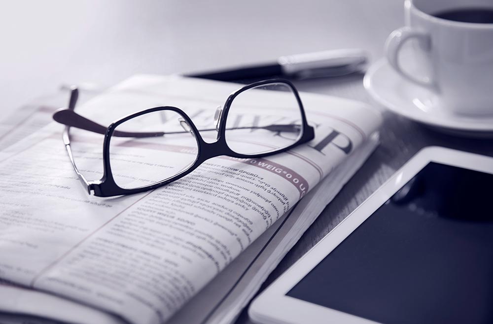 Black and white shote of table with glasses and newspaper and coffee and tablet on top